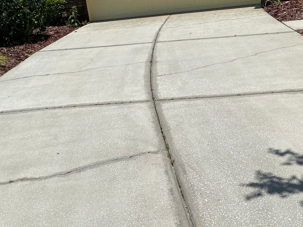 Concrete driveway after exterior cleaning, with existing cracks still visible.